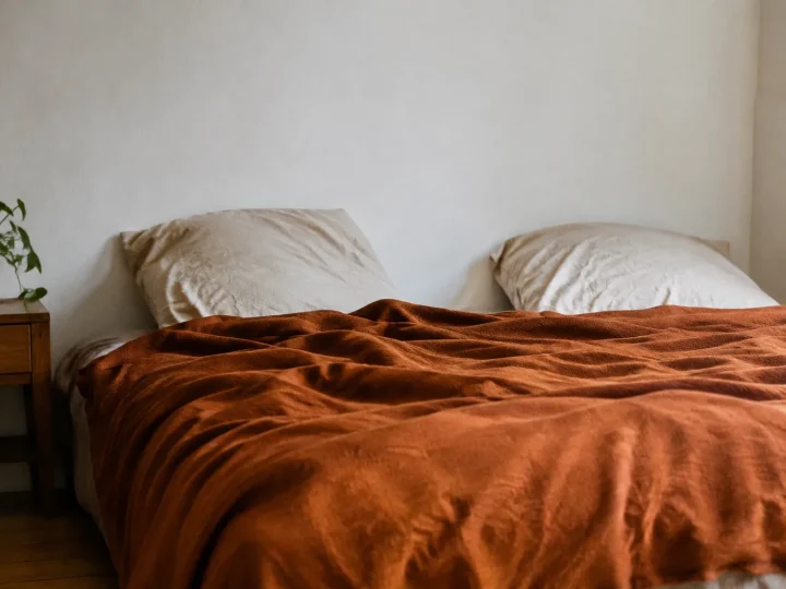 Lit bas recouvert plaid orange brique devant mur blanc